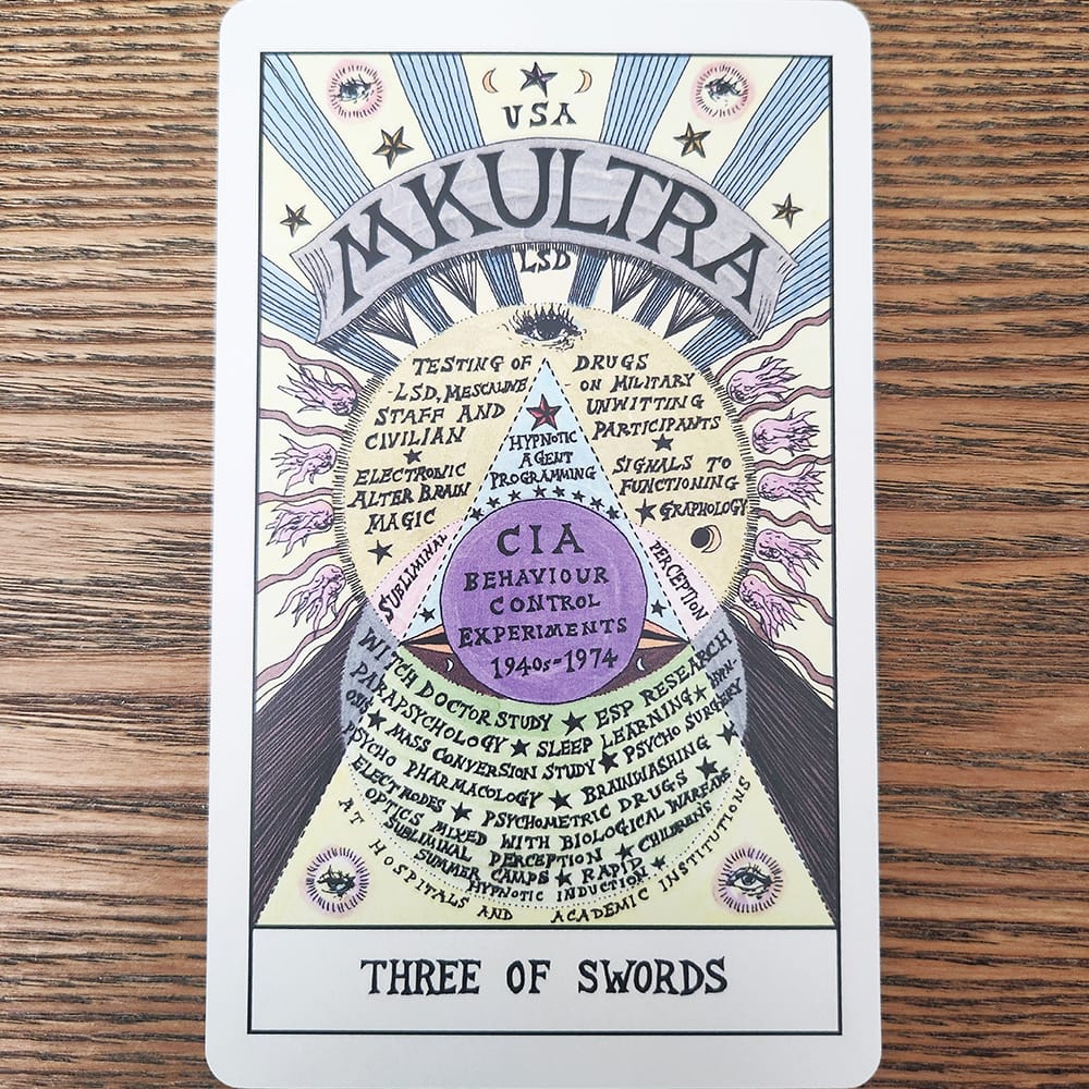 A three of swords tarot card showing a banner that reads MKULTRA across the top, with associated words below spanning the rest of image.
