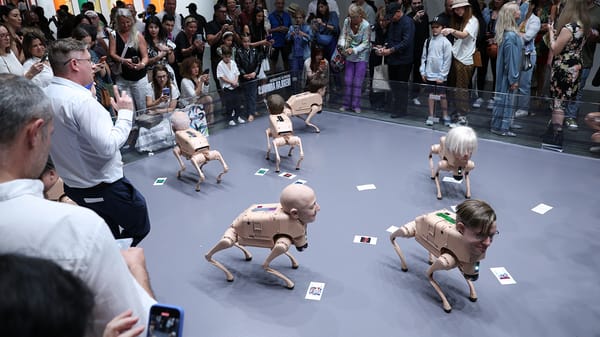 A crowd of people gather around an art exhibit of robot dogs with human heads.